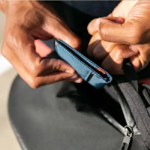 Hands taking a light blue vegan minimalist slim wallet out of a black backpage.