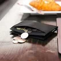 Picture shows a wallet on a table with a coin pocket, and coins spilling from the thin black wallet.