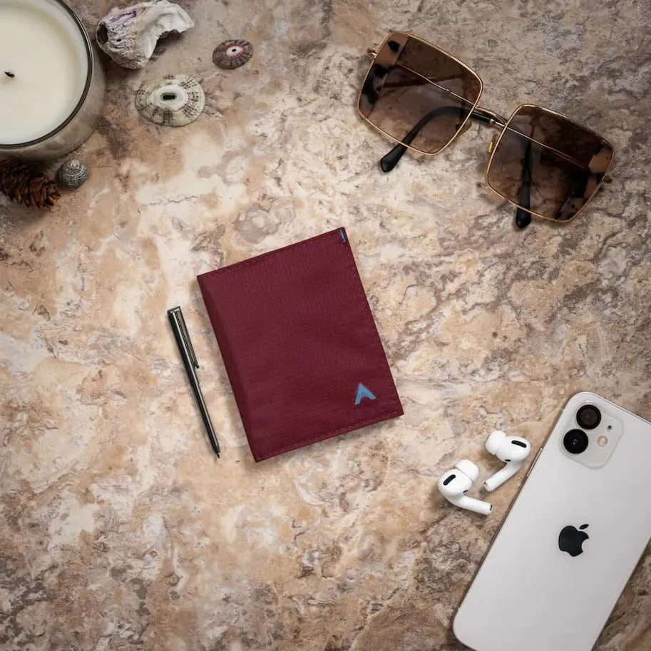 Mulberry wallet set against a tan table with glasses and a phone surrounding it. Allett Hybrid Card Wallet mulberry