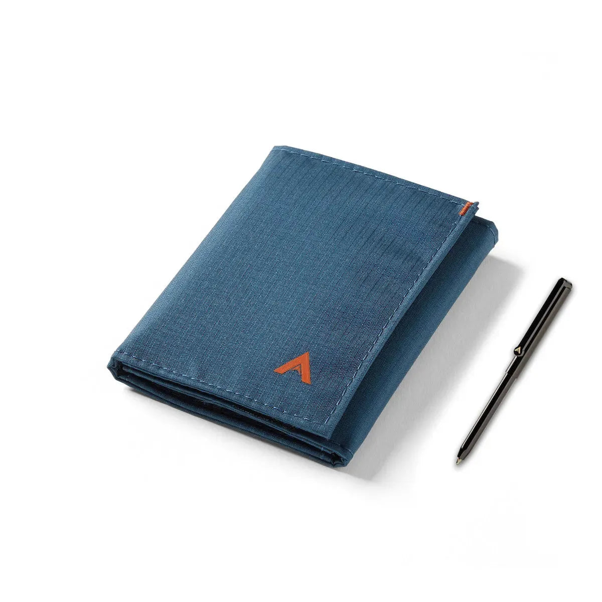 Vegan ripstop nylon trifold wallet in indigo blue, resting closed beside a silver micro pen, contrasted against a white background. Allett Trifold Wallet nylon edition - indigo-blue - pen