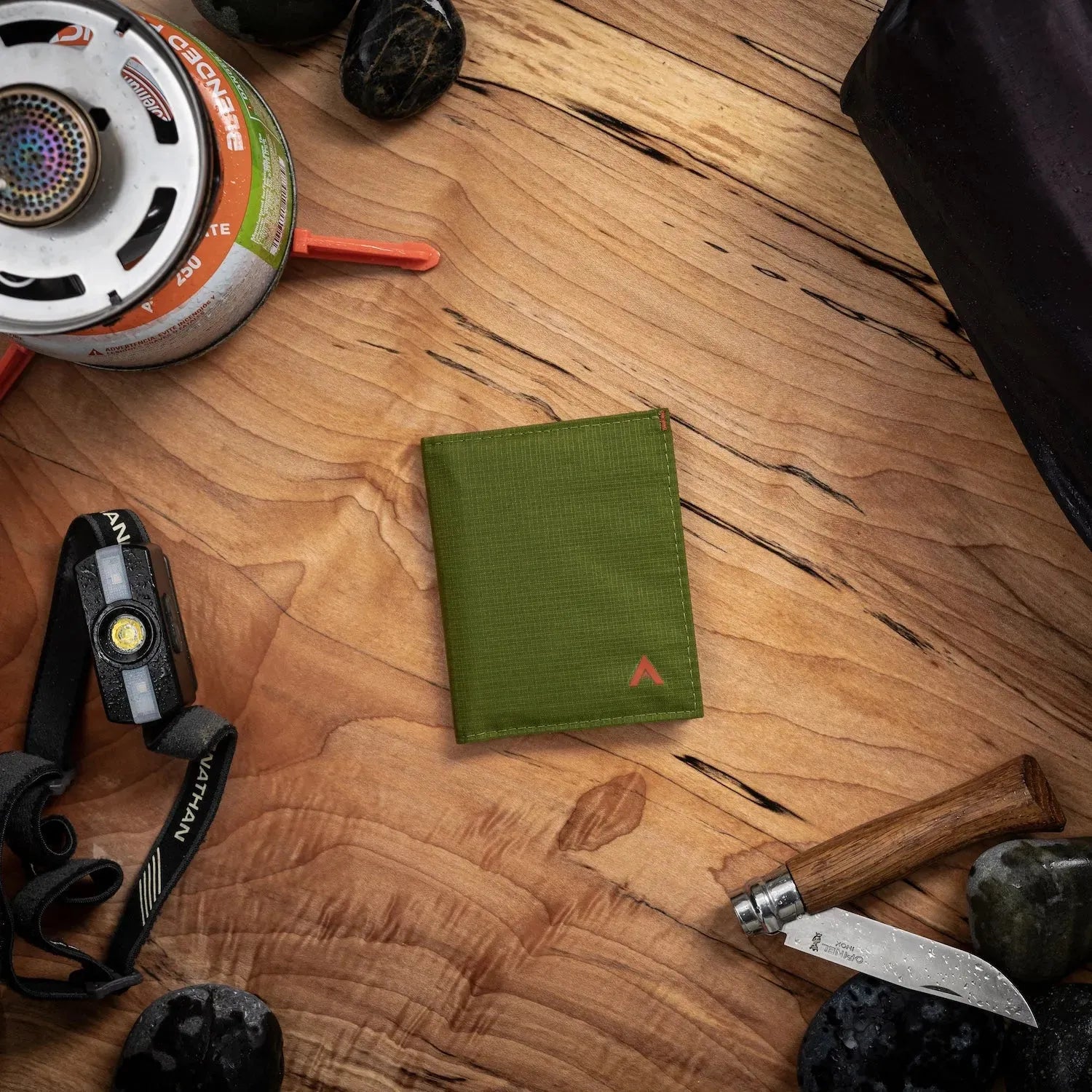 Cala Green hybrid card wallet from Allett, presented on a wood table with everyday outdoor items like a pocket knife. Allett Hybrid Card Wallet cala-green