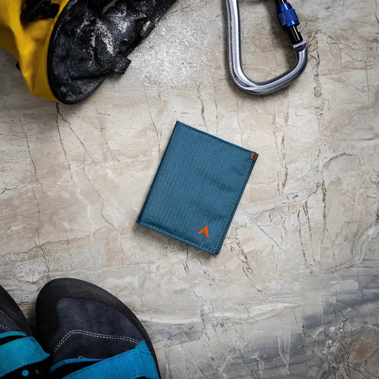 Indigo blue hybrid wallet against an offwhite table surrounded by outdoor gear and items. Allett Hybrid Card Wallet indigo-blue