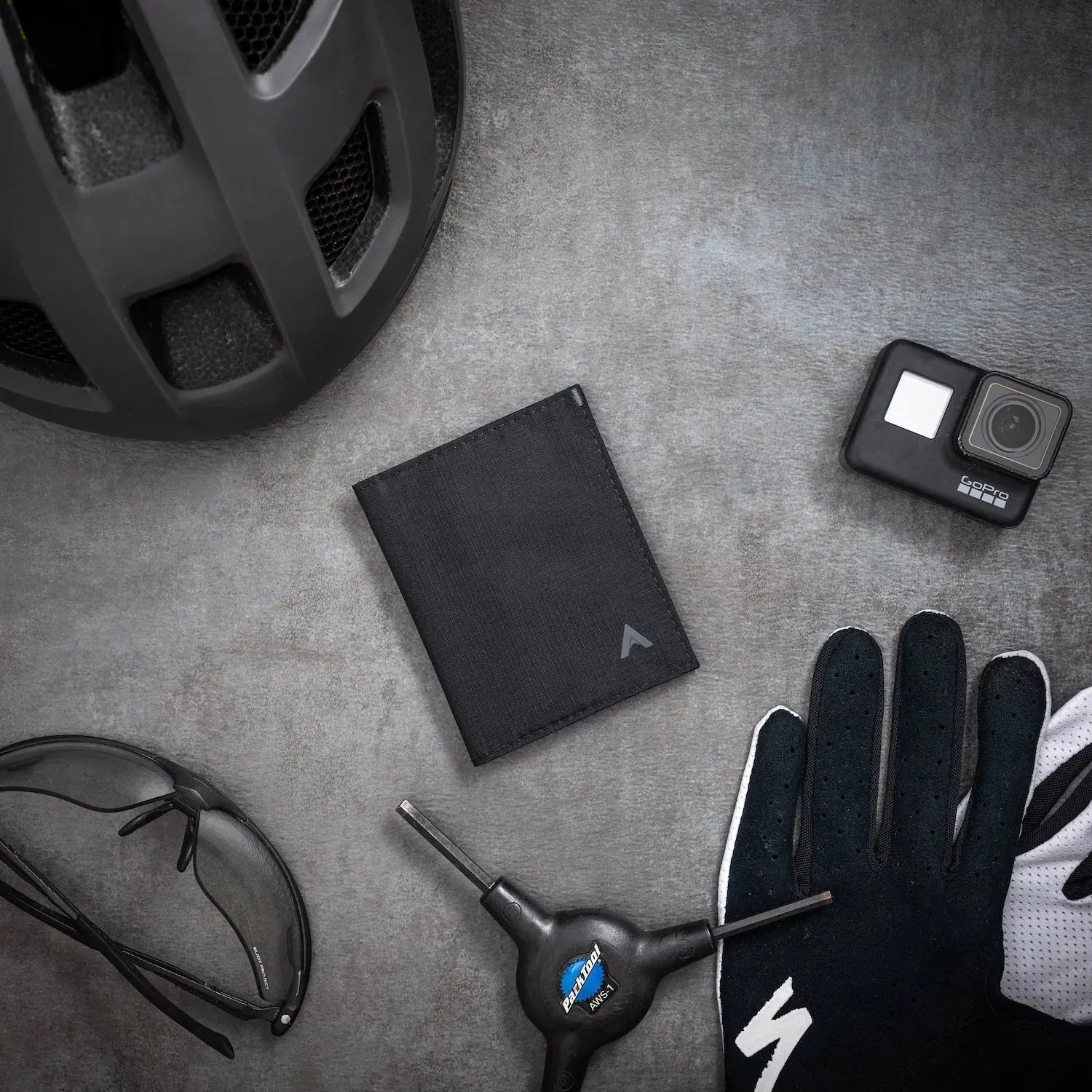 Jet black hybrid wallet on a grey background surrounded by other black outdoor items like gloves. Allett Hybrid Card Wallet jet-black