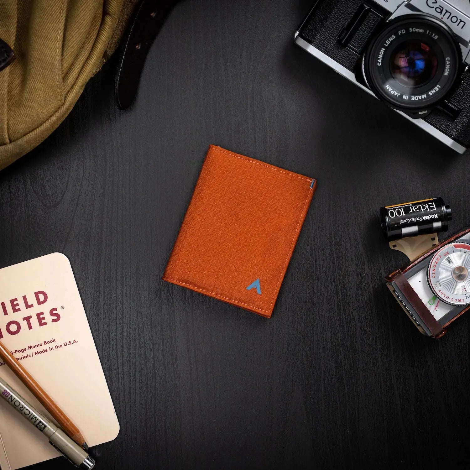 Potters clay vegan nylon card wallet on a black table surrounded by items a person may carry, such as a camera. Allett Hybrid Card Wallet potters-clay