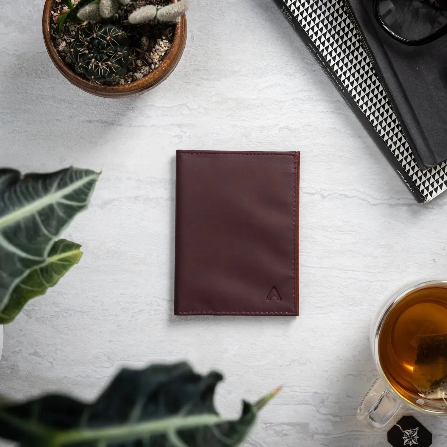 Allett's Nappa leather wallet in merlot color sitting against an offwhite table, surrounded by household items. Allett leather original wallet merlot