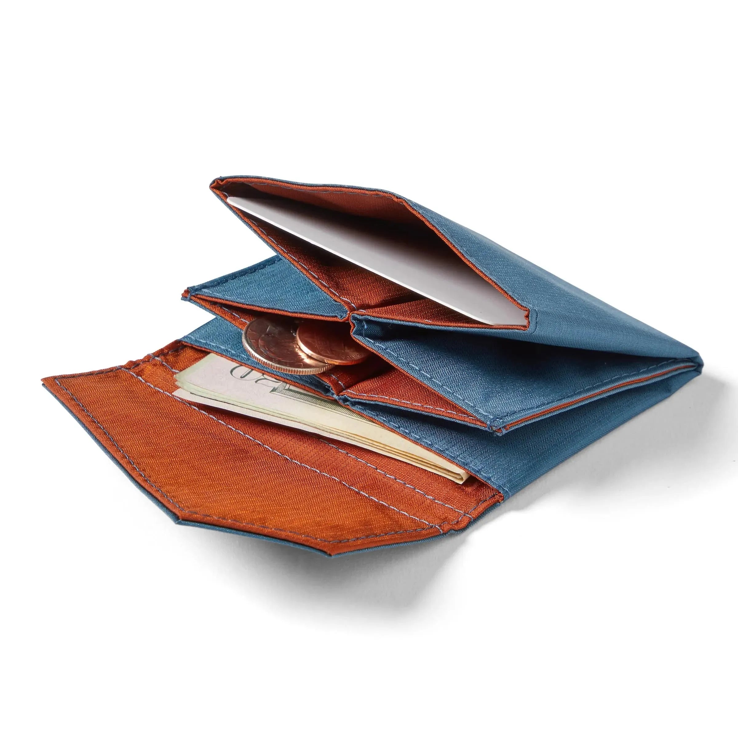 Allett's premium indigo blue nylon accordion wallet with a slightly orange interior lying open on a white backdrop, with cash and coins slightly extending from the inner pockets. Allett Accordion Wallet in RFID Blocking Nylon indigo-blue
