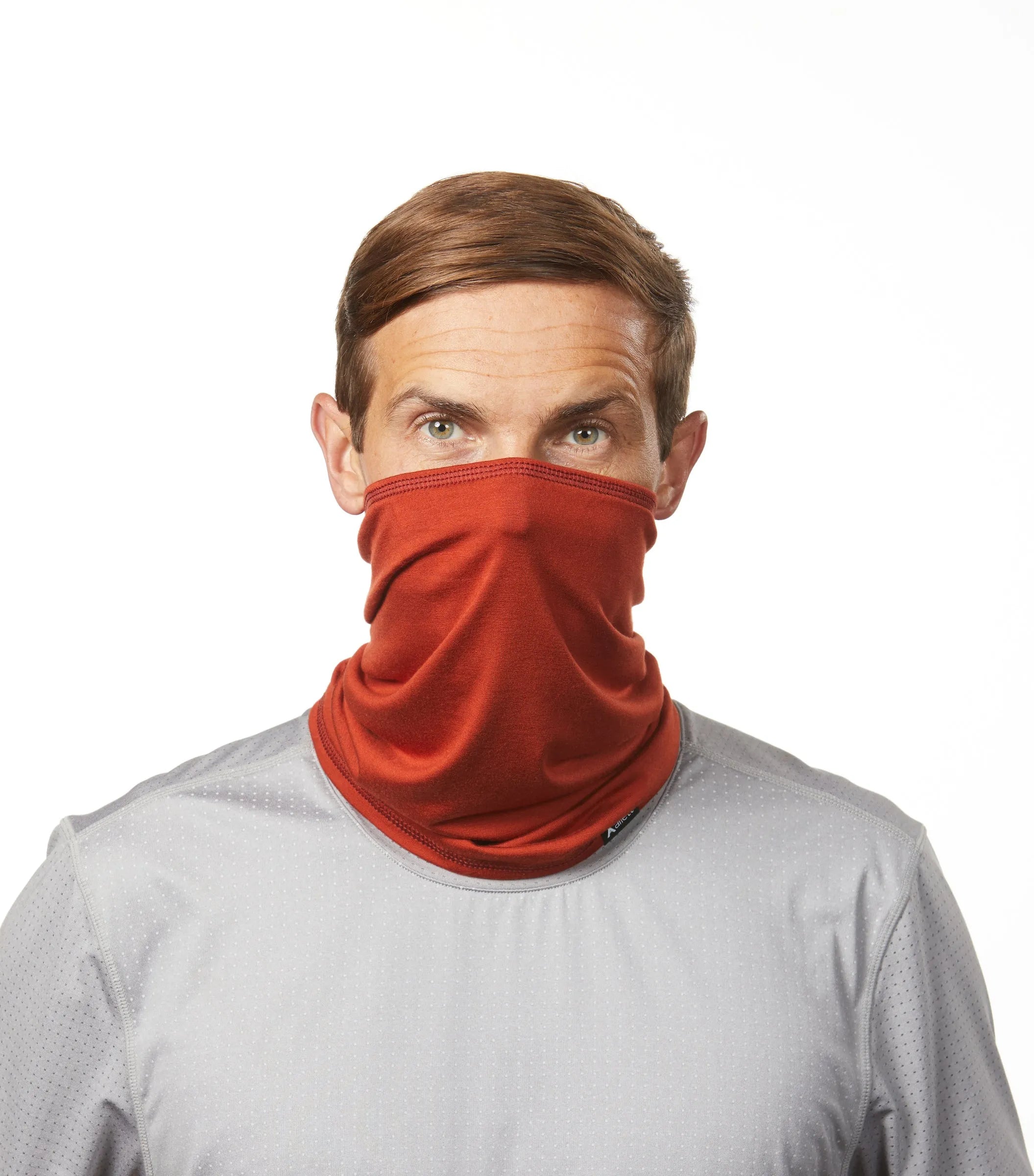 Photo of a man facing the camera wearing a reddish rust colored neck gaiter made with sustainable fabric. rust