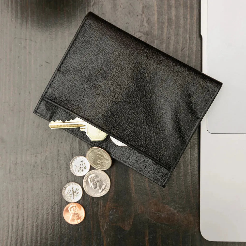 Coins and a key spilling out of the onyx black Nappa leather wallet from Allett. allett leather coin wallet onyx-black