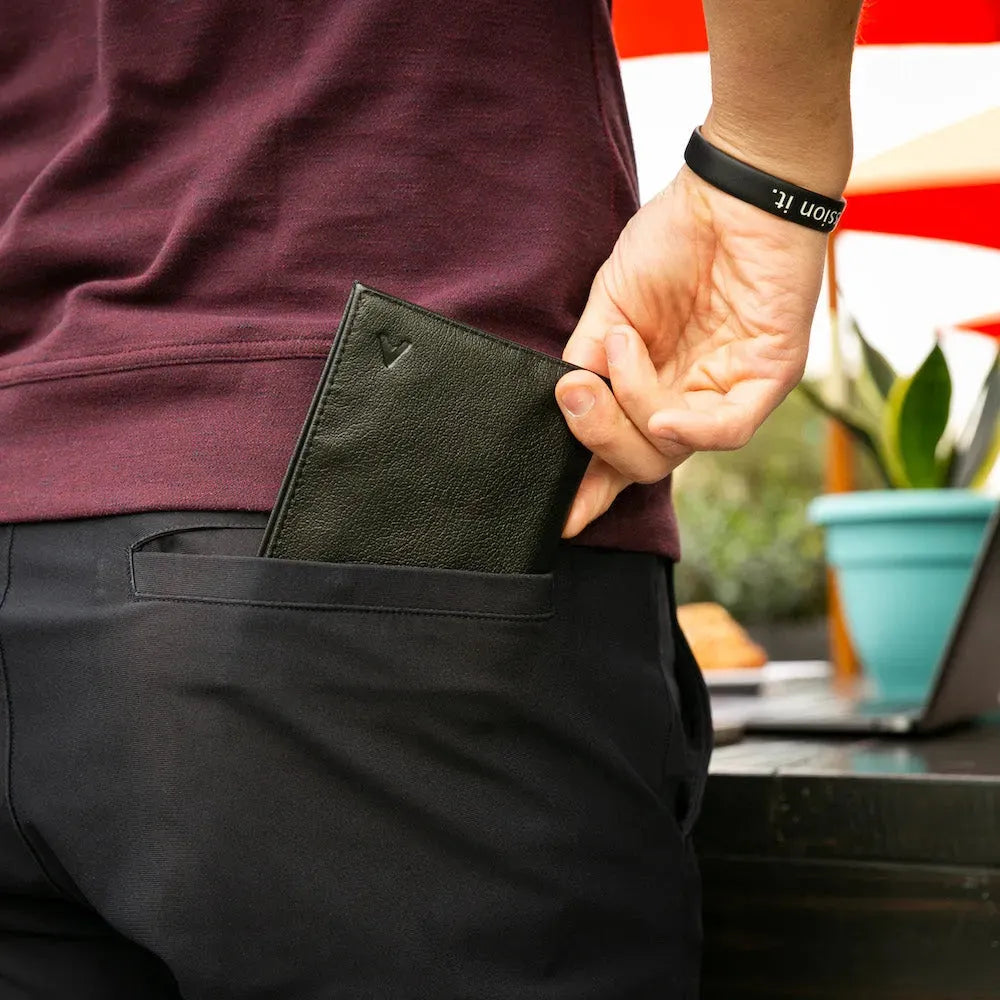 Man in a maroon shirt and black pants pulling a black leather slim wallet from his back pocket. Allett leather original wallet onyx-black