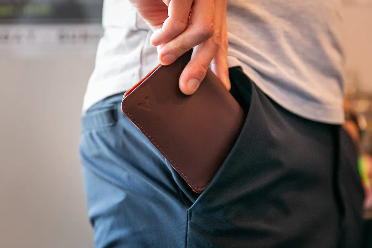 Man putting a thin brown leather wallet into his front pocket.