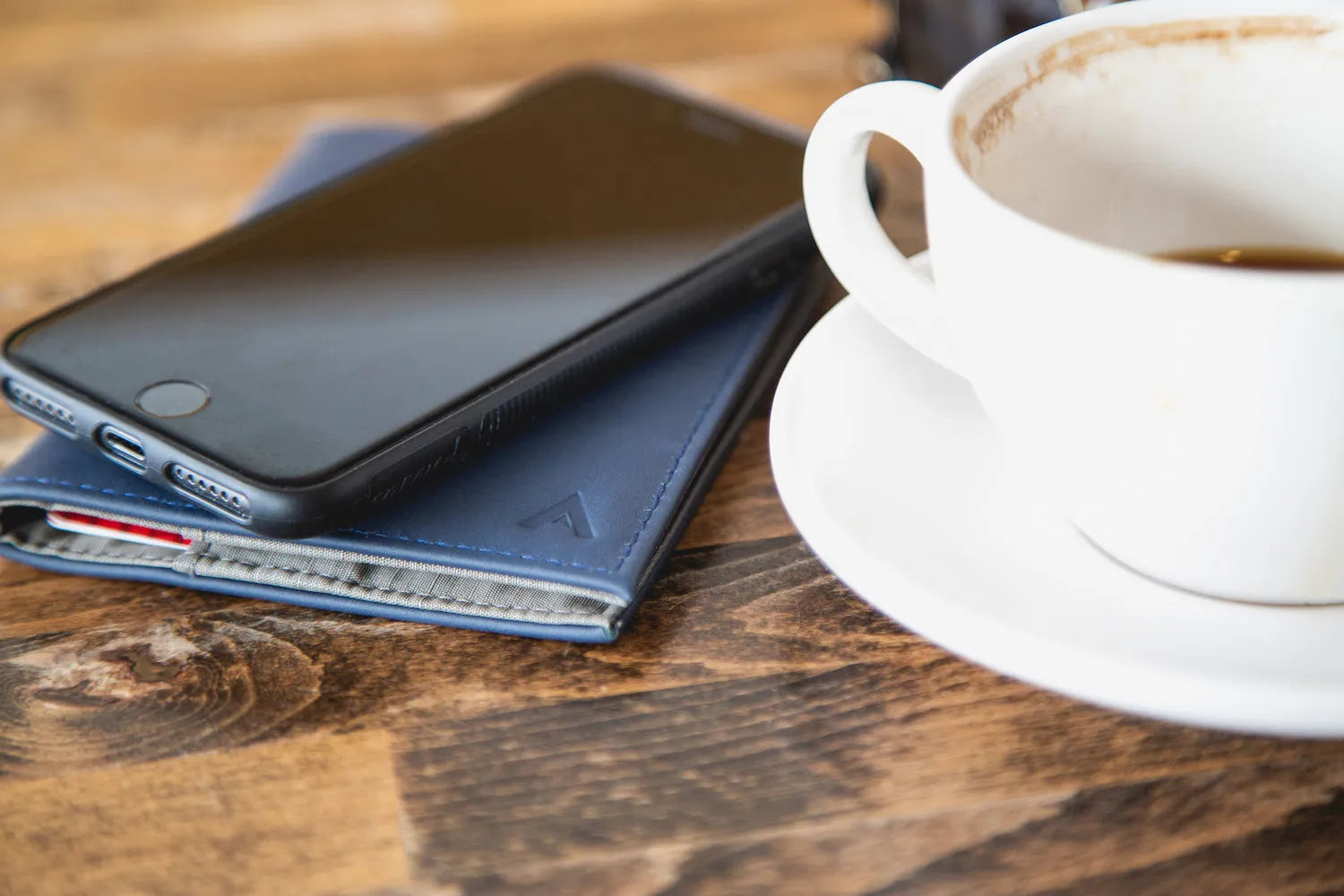 Image of a cell phone sitting on top of a slim blue wallet.