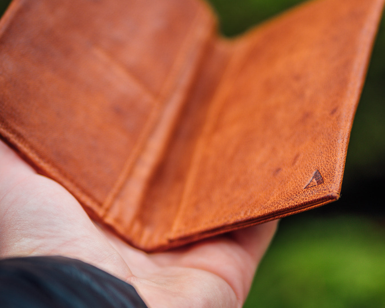 Gently used light brown mans leather wallet held out in the palm of a man's hand.