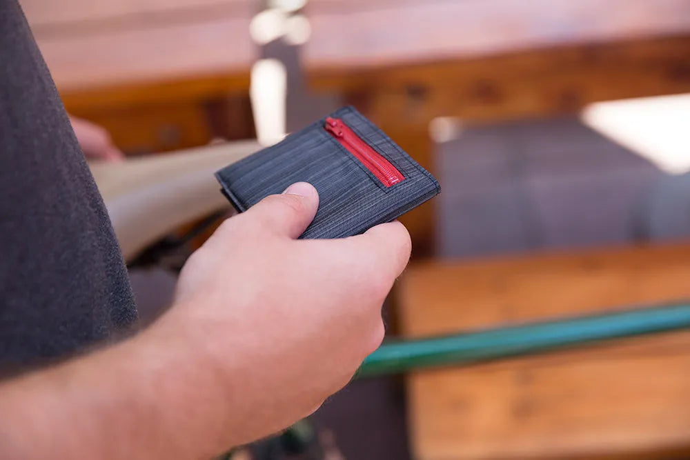 Man holding a dark wallet with a vibrant red zipper.
