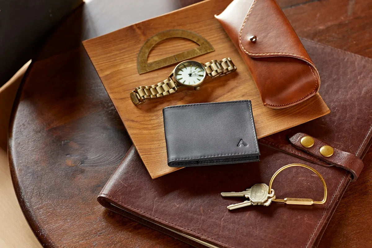 Black leather wallet sitting on a table next to a watch.