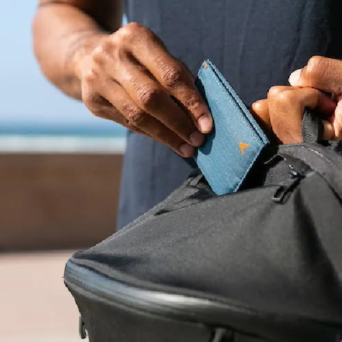 Allett Wallets photo shows a man placing a light blue wallet into his bag.