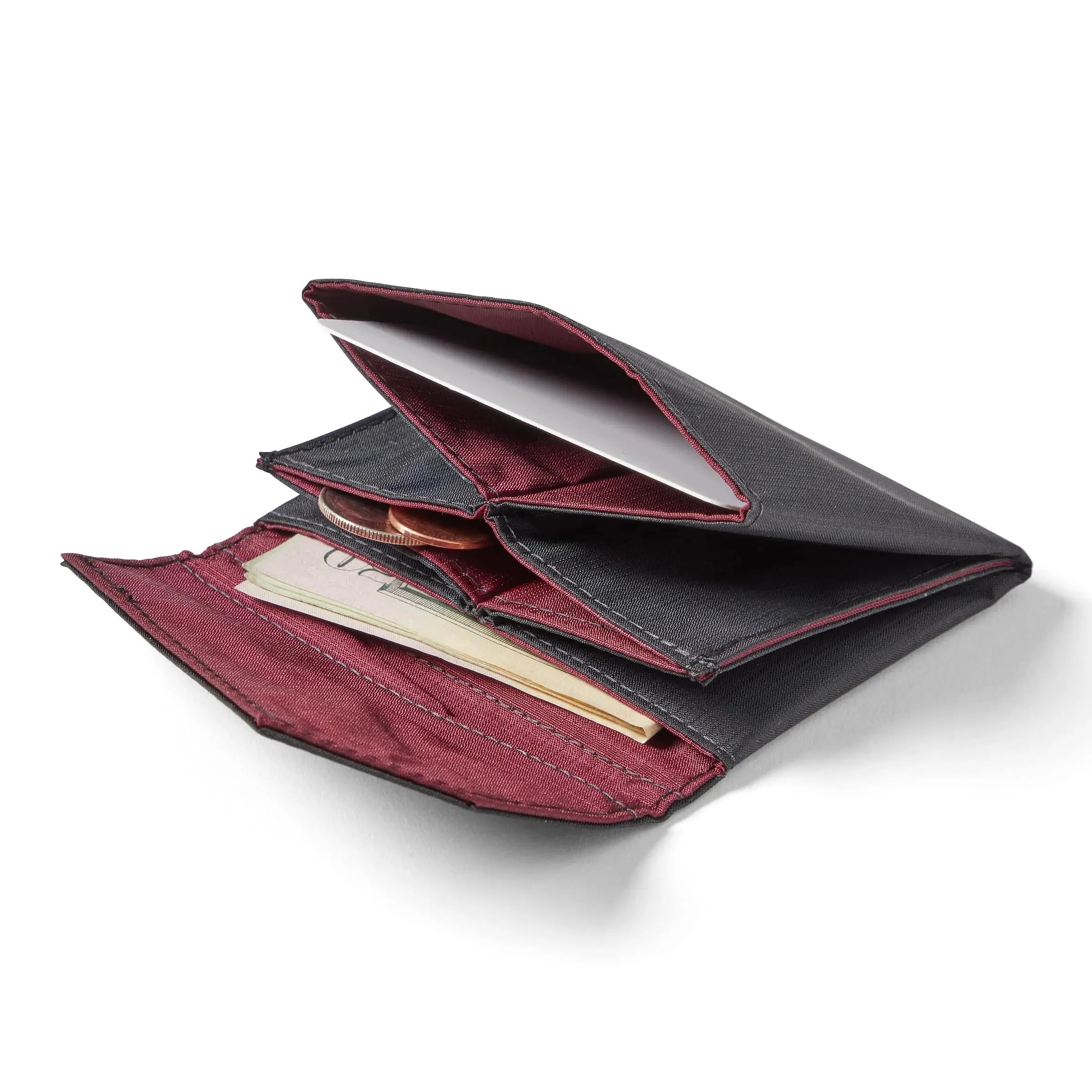 Allett's jet black ripstop nylon accordion wallet spread flat on a white surface, with coins and bills peeking out from the pockets. Allett Accordion Wallet in RFID Blocking Nylon  jet-black