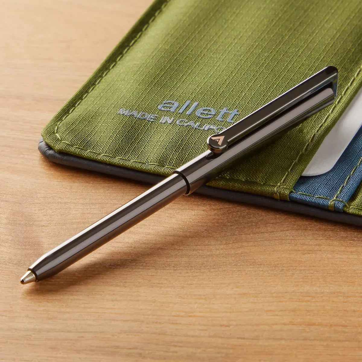 Allett Micro Wallet Pen sitting next to wallet, brass with a gunmetal finish