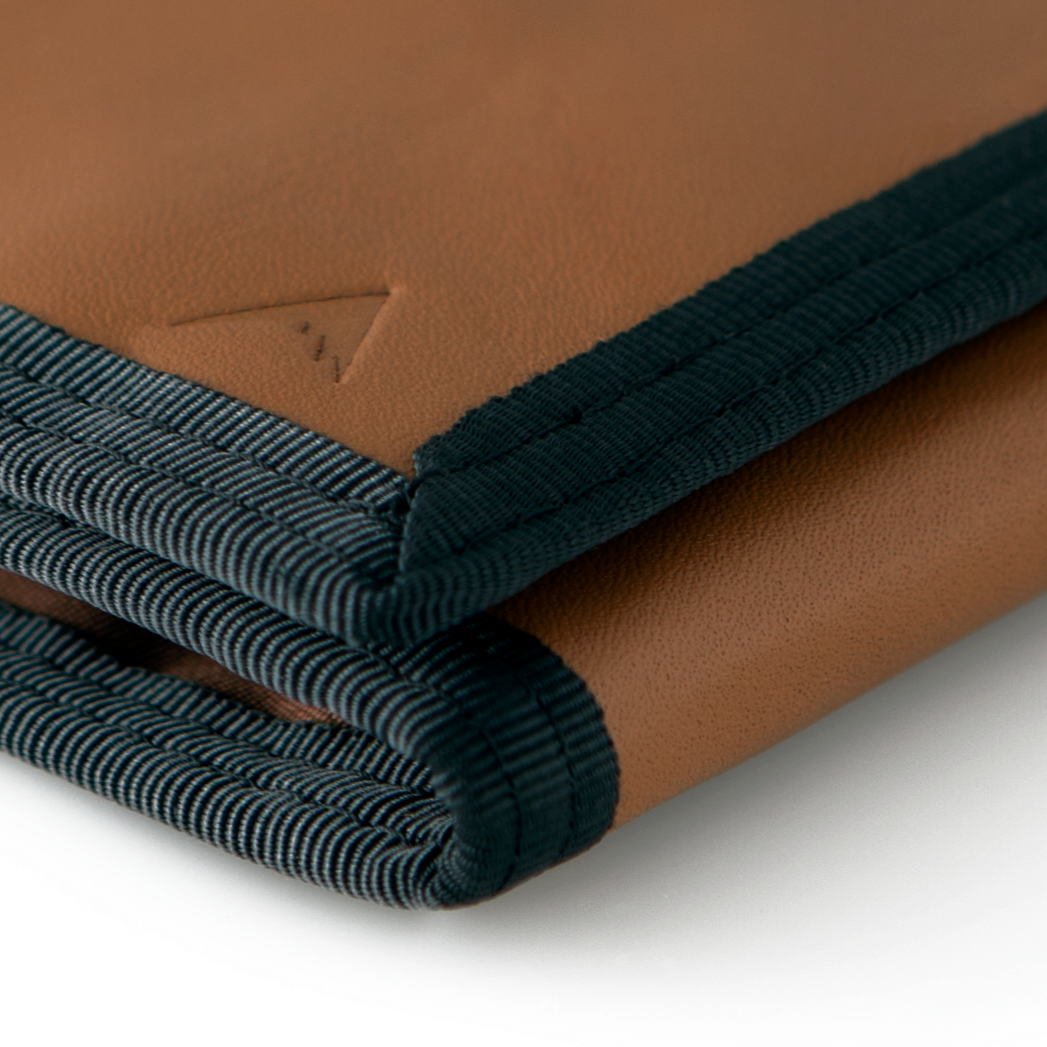 Detailed focus on the defined corner of the brown leather "Switchback" trifold wallet with trim, with the Allett logo in sight. Allett Switchback Leather Wallet - brown