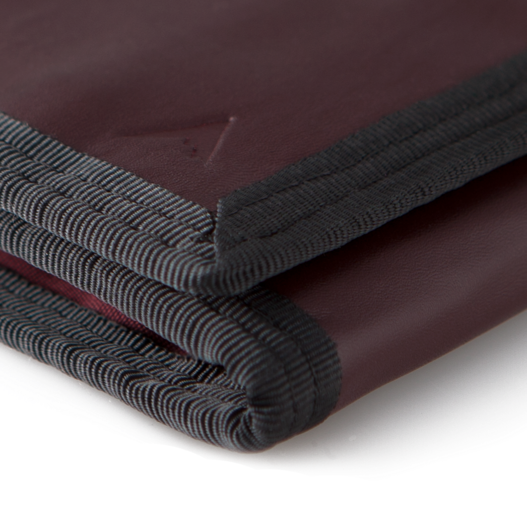 Zoomed-in view of the prominent corner of the oxblood leather "Switchback" trifold wallet, centering on the Allett logo. Allett Switchback Leather Wallet - oxblood